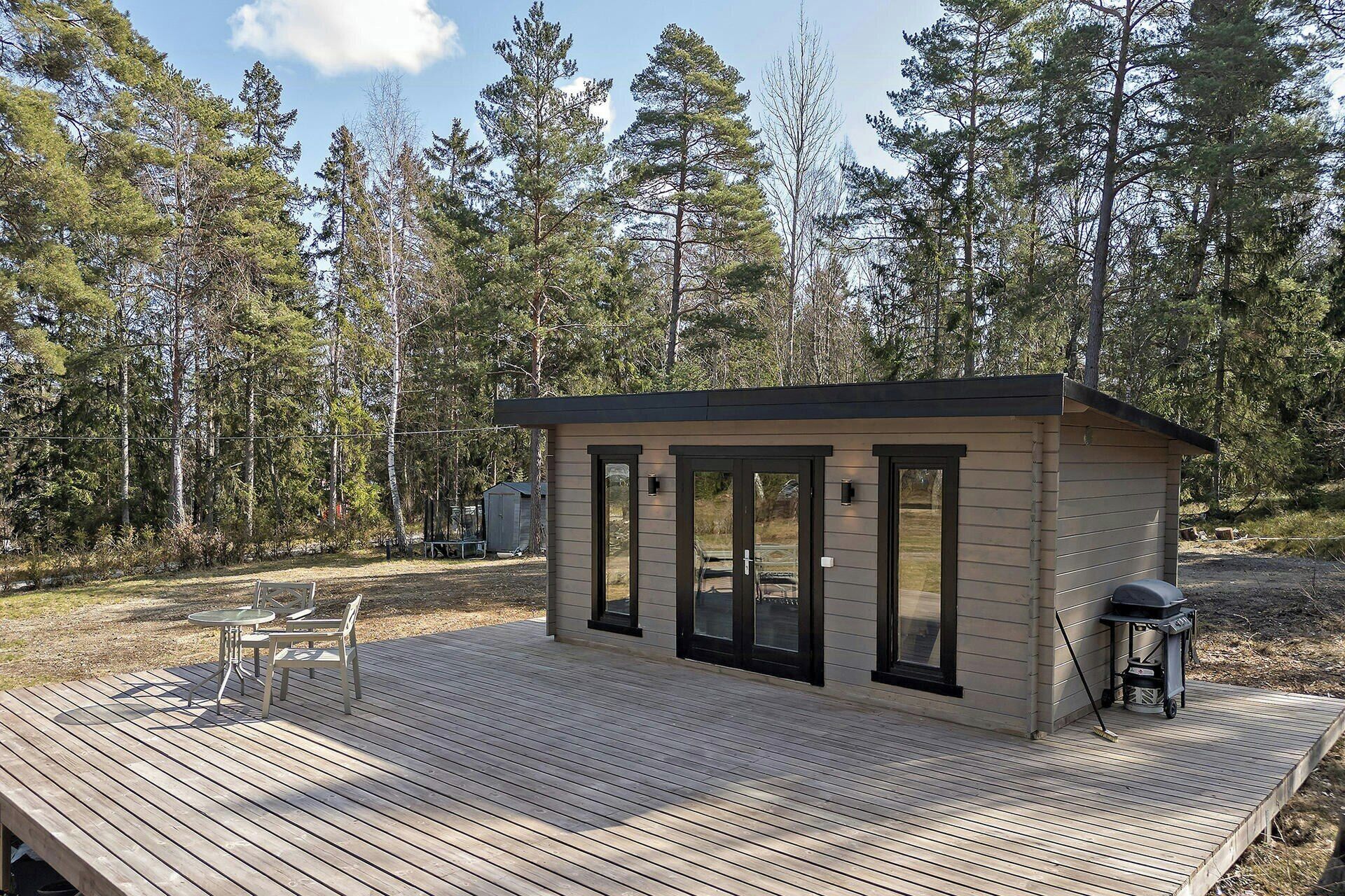 Une petite cabane avec une terrasse, un barbecue et un abri de jardin, située dans une zone boisée.
