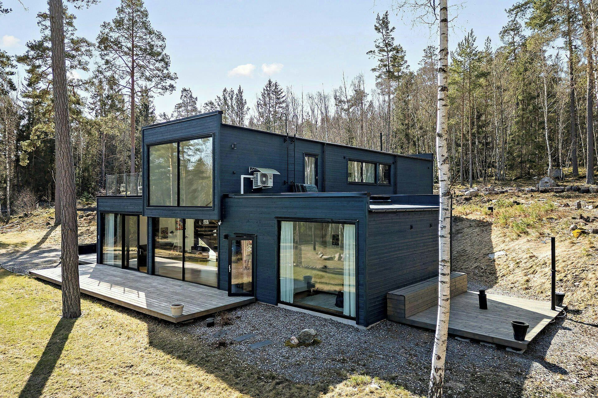 A modern, multi-level cabin with large glass windows, surrounded by a forest.