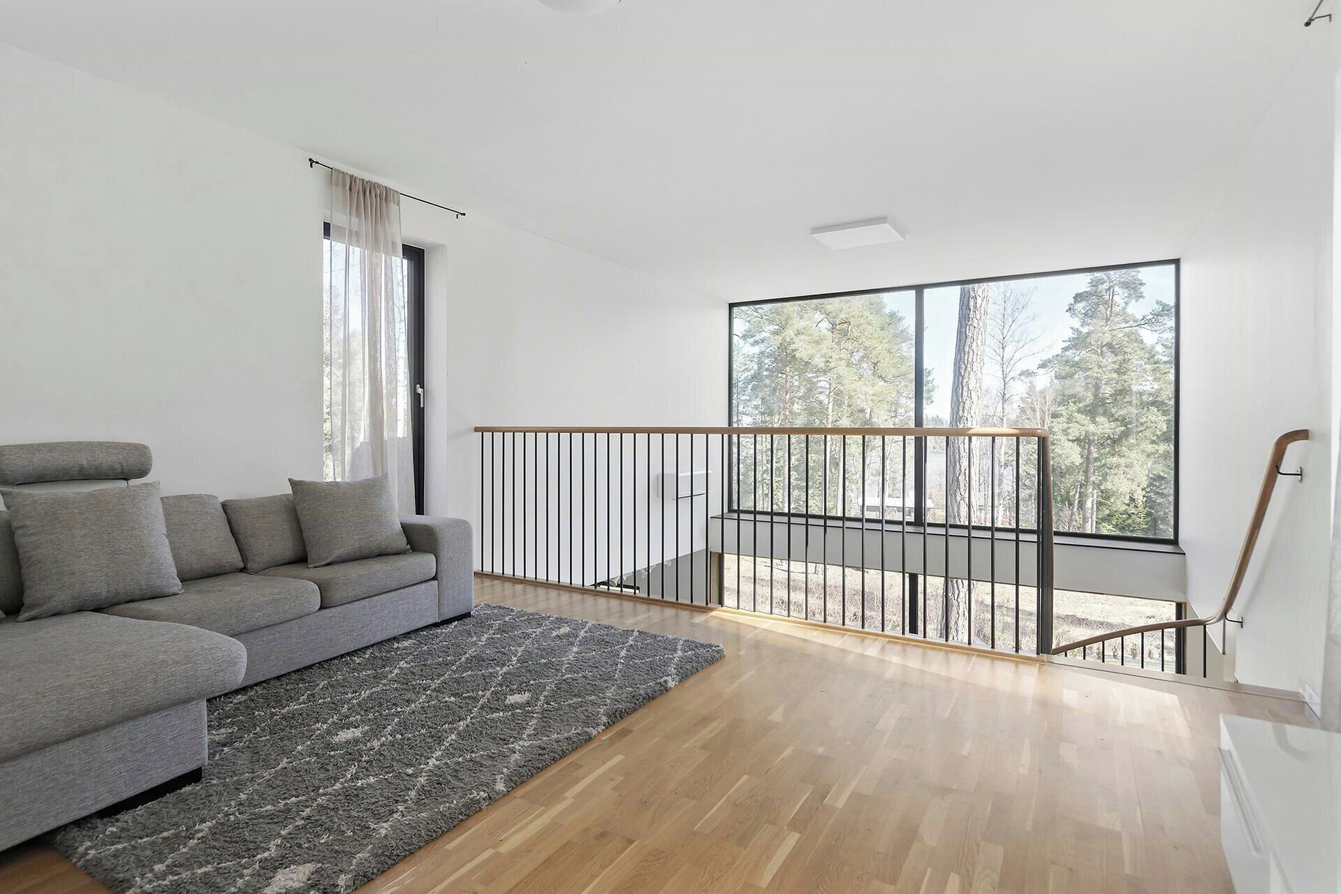 A modern living room with a grey sofa, a patterned rug, and a wooden floor.