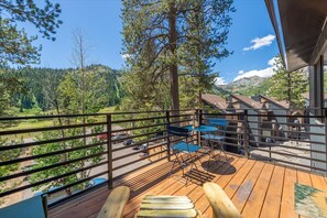 A wooden deck with a view of a mountainous landscape, a table with chairs, and a railing. - Alpenglow Loft | Palisades Adventure Basecamp (Olympic Valley)