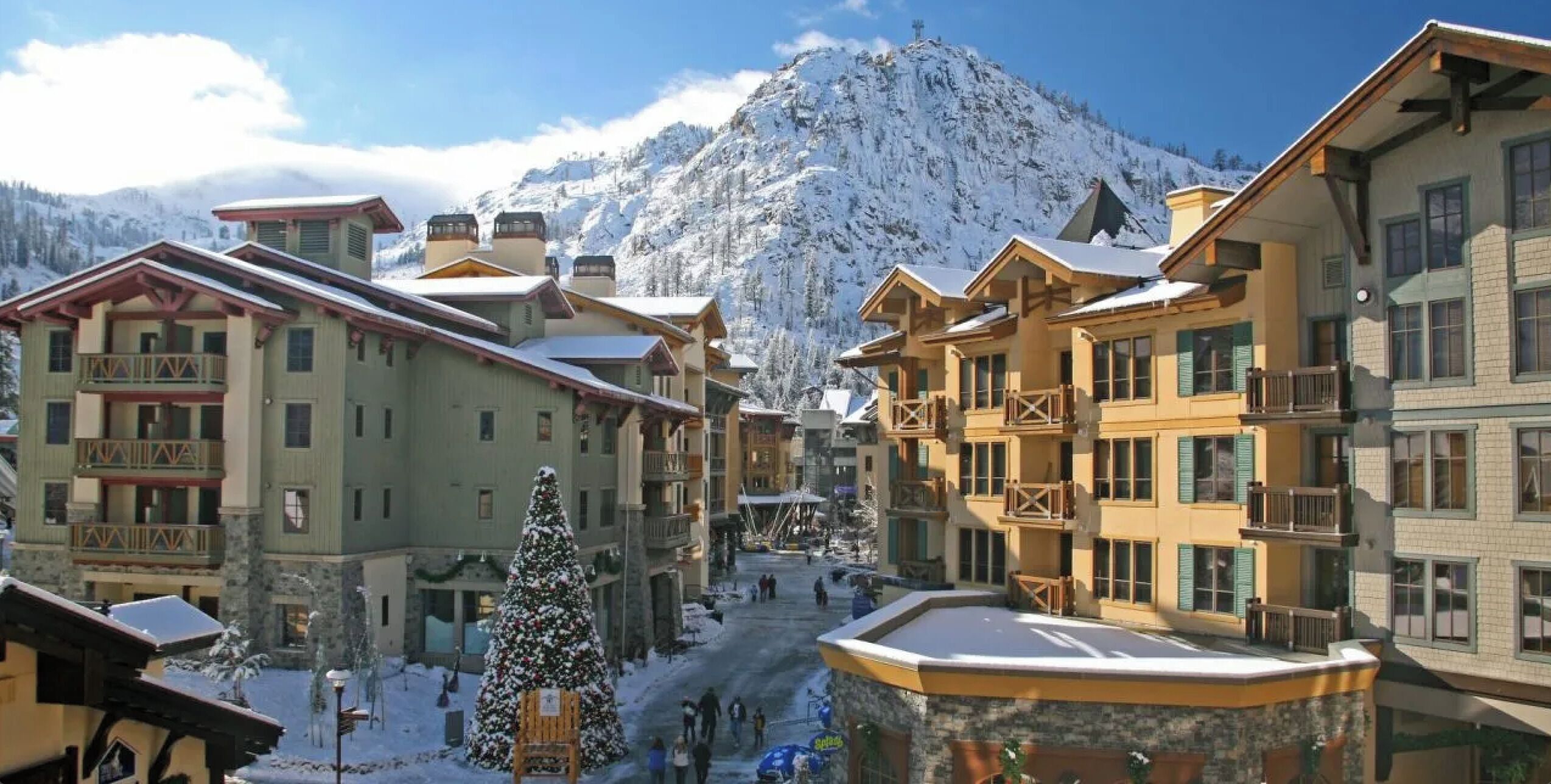 A snow-covered mountain town with multi-story buildings, a central pedestrian area, and a prominent snow-covered tree.