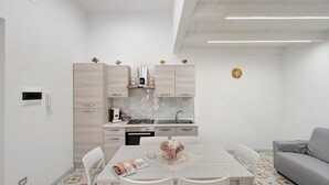 Cocina moderna con gabinetes blancos, una mesa de comedor y un sofá gris.
