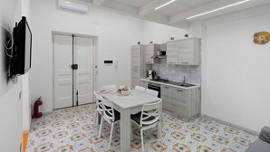Una cocina compacta con armarios blancos, una mesa de comedor con sillas, una pequeña isla y piso de baldosas.