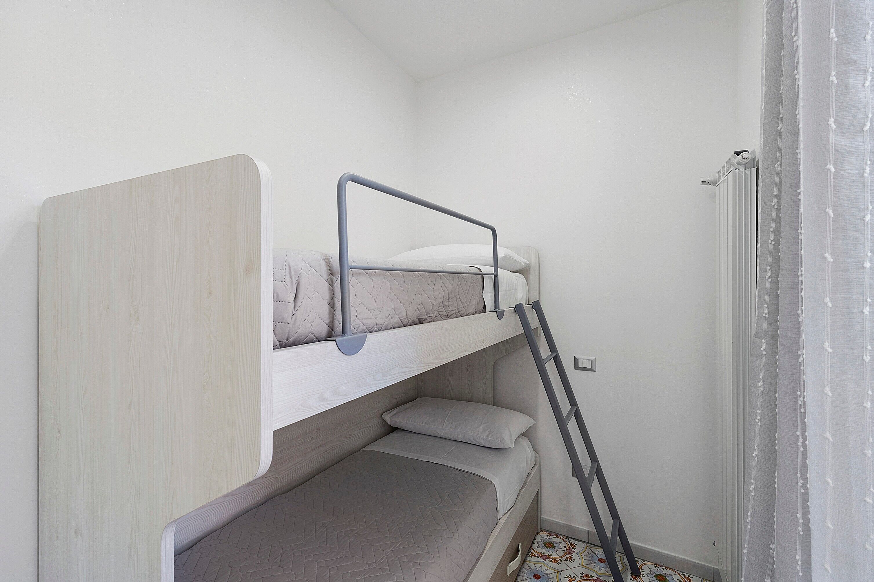 Uma cama beliche com escada, uma mesinha de cabeceira e um aquecedor fixado na parede.