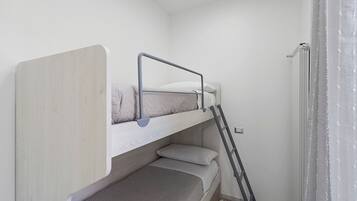 Uma cama beliche com escada, uma mesinha de cabeceira e um aquecedor fixado na parede.