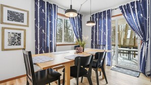 A dining area with a wooden table, black chairs, blue curtains with tree patterns, and pendant lights. - Pocono Lake House - Short Walk to All Amenities! (Albrightsville)