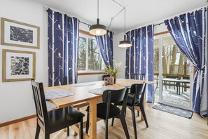 A dining area with a wooden table, black chairs, blue curtains with tree patterns, and pendant lights. - Pocono Lake House - Short Walk to All Amenities! (Albrightsville)