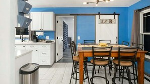 Uma cozinha compacta com armários brancos, uma mesa de jantar com cadeiras e um lustre no teto.