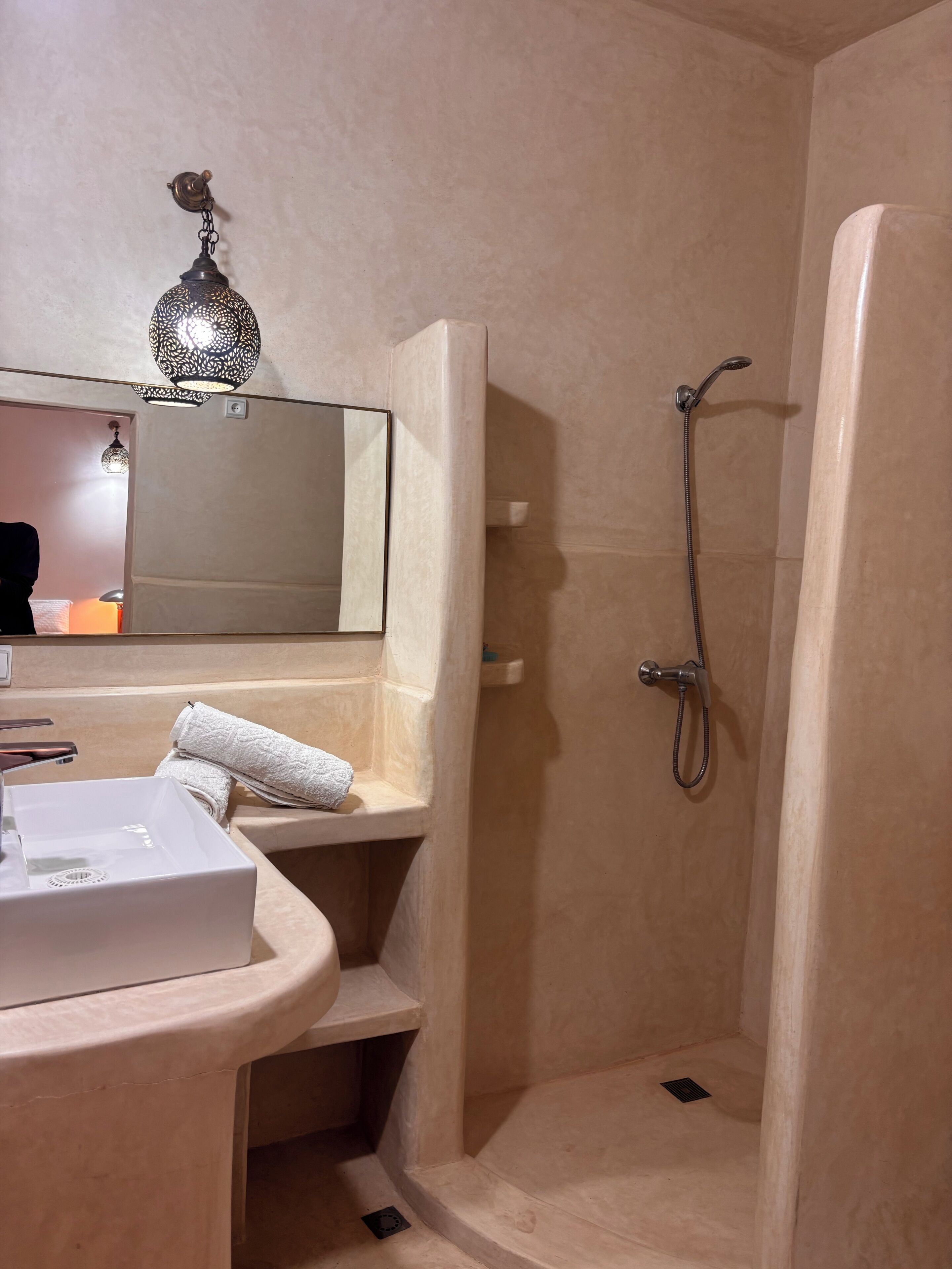 Ein Badezimmer mit Waschbecken, Spiegel, Handtuch, Dusche und einer dekorativen Leuchte.