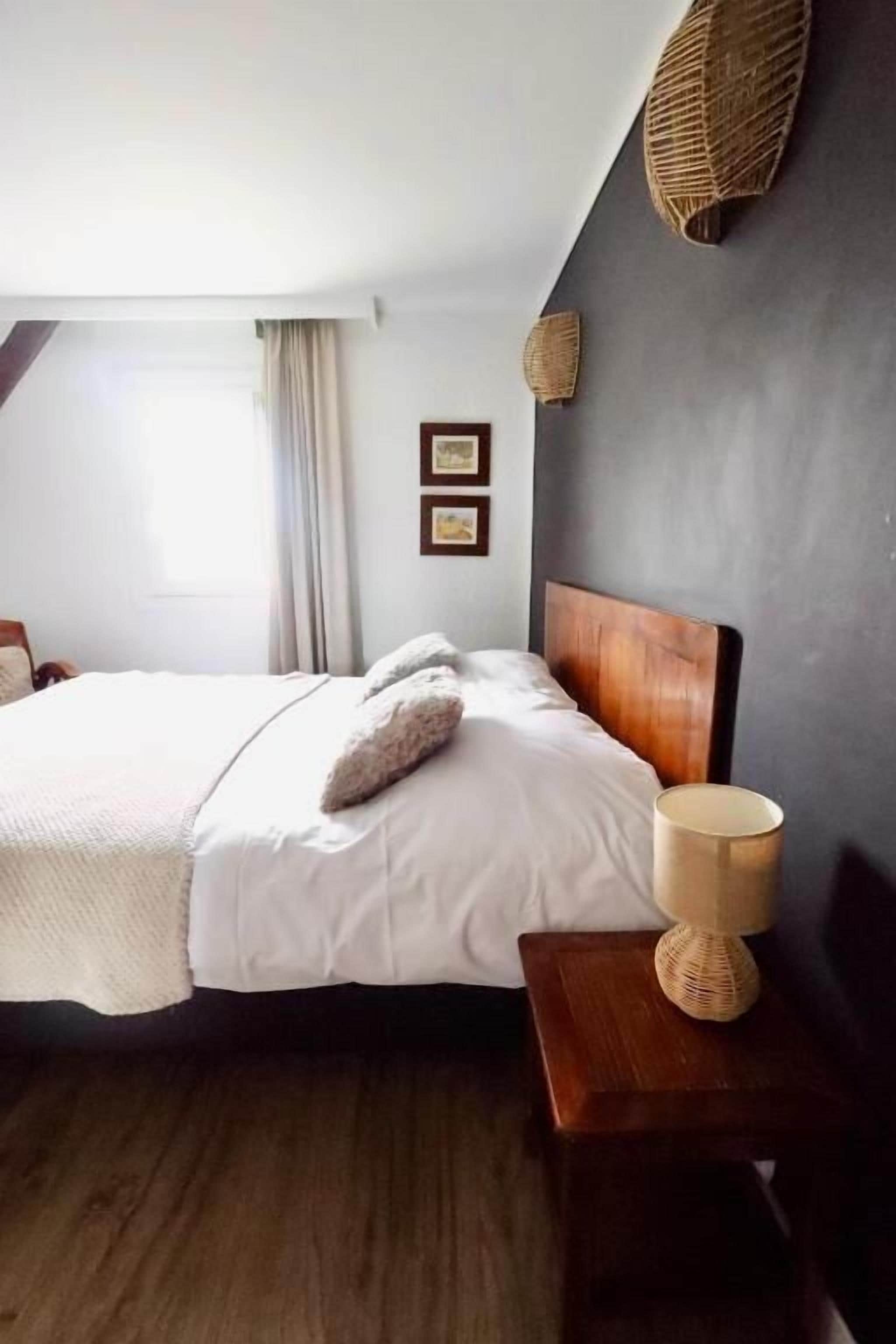 Een slaapkamer met een bed, een bedlamp, een raam met gordijnen en een wandplank.