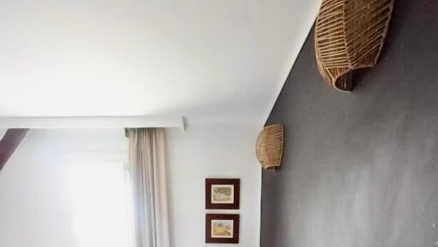Un dormitorio con cama, lámpara de noche, ventana con cortinas y estante en la pared.