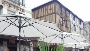 Un café al aire libre con mesas y sombrillas, rodeado de edificios con letreros visibles.