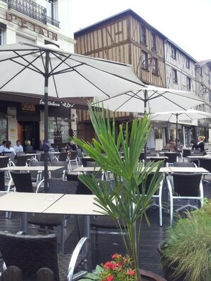 An outdoor café with tables and umbrellas, surrounded by buildings with visible signage. - POT D'ÉTAIN (Châlons-en-Champagne)