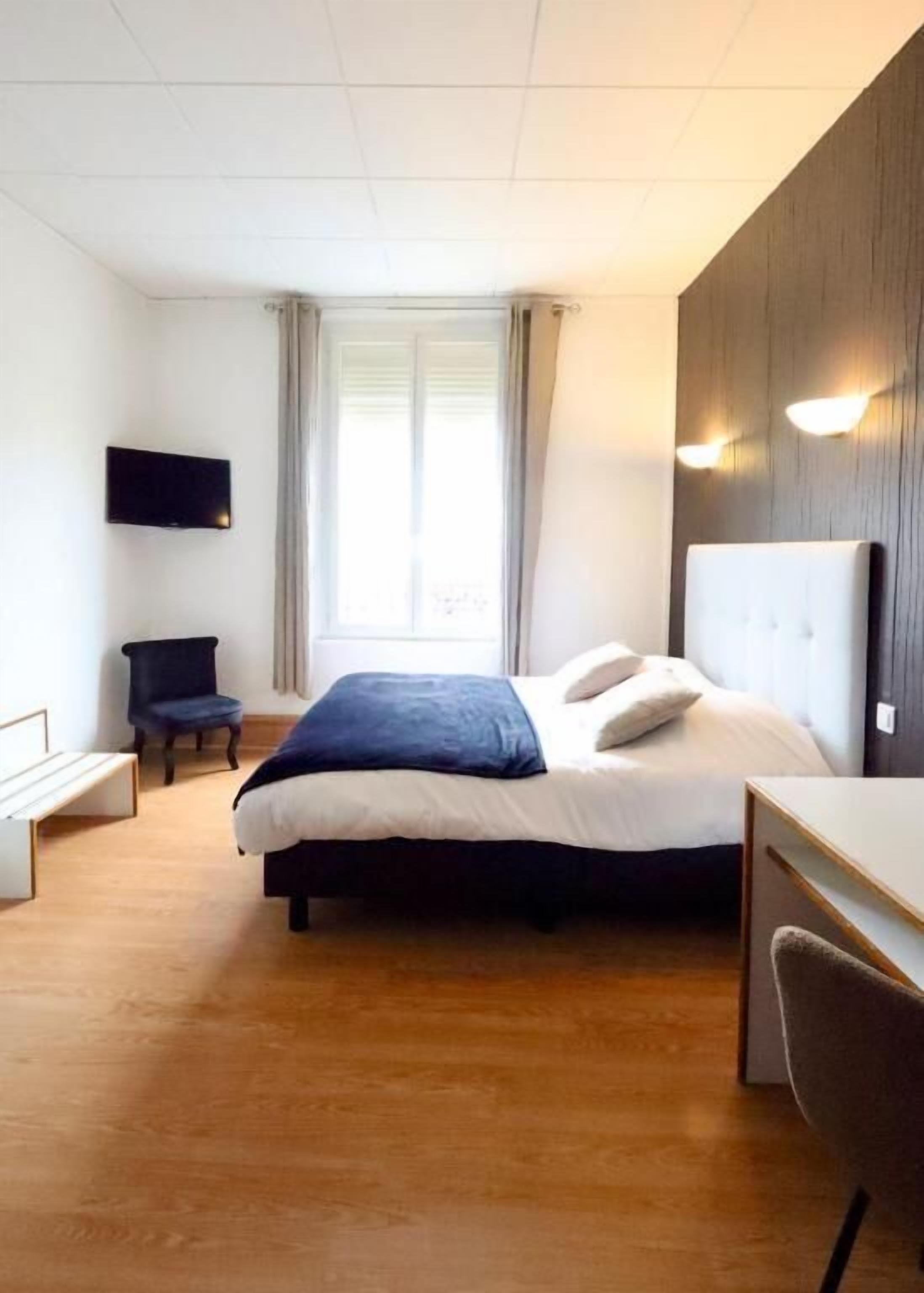 A hotel room with a bed, a desk, a chair, a TV, and a window with curtains.