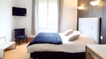 A hotel room with a bed, a desk, a chair, a TV, and a window with curtains.