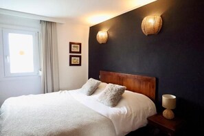 A hotel room with a bed, two wall-mounted lamps, a window with curtains, and a nightstand with a lamp. - POT D'ÉTAIN (Châlons-en-Champagne)