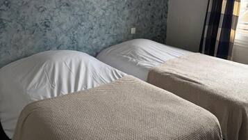 Een kamer met twee bedden, een behang met patroon en een raam met gordijnen.