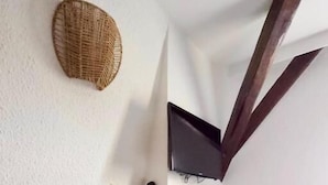 Una habitación con una mesa de madera y dos sillas, un televisor instalado en la pared y una cesta tejida en el techo.