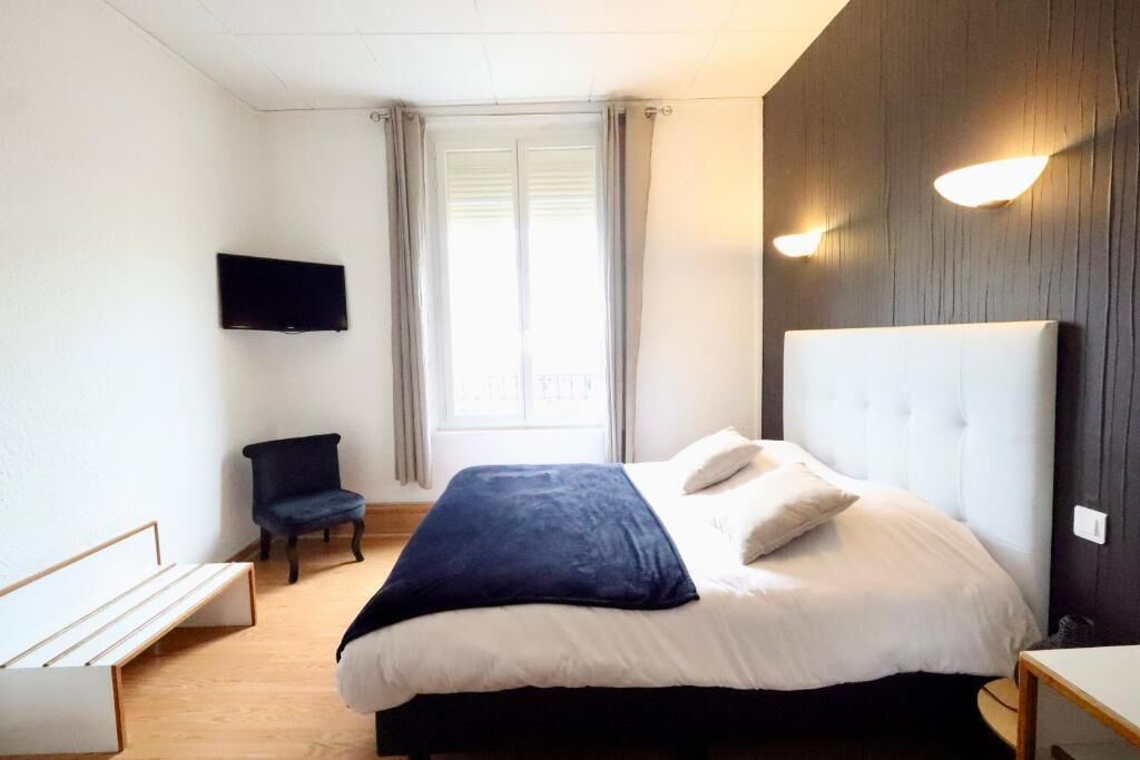 Un dormitorio con cama, una silla, televisión y ventana con cortinas.