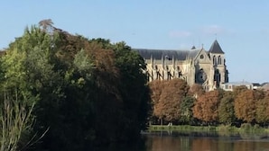 Un edificio histórico con una torre de reloj, ubicado junto a un lago tranquilo con árboles en primer plano.