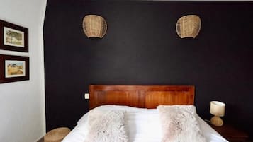 Un dormitorio con una pared oscura, un cabecero de madera, dos almohadas blancas y mullidas, y dos adornos de pared hechos con fibras naturales.