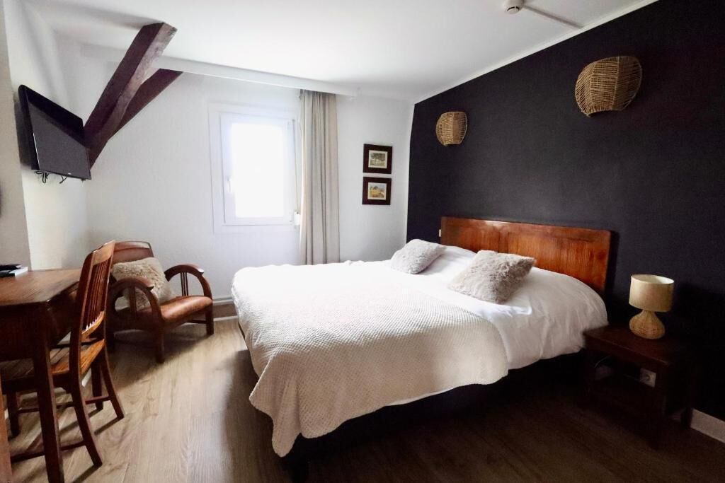 A bedroom with a bed, wooden headboard, bedside table, lamp, and a window with curtains.