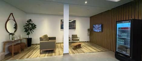 A reception area with a sofa, chairs, a coffee table, a refrigerator, and a television.