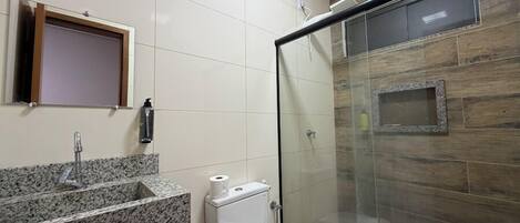 A bathroom with a granite countertop sink, a toilet, and a glass shower enclosure.
