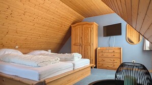 Quarto com teto inclinado, cama, guarda-roupa, penteadeira, mesa redonda e uma cadeira.
