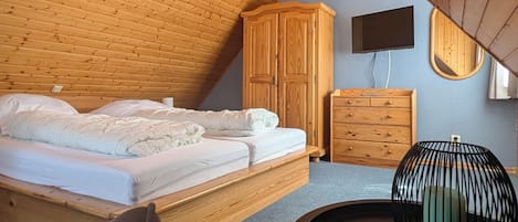 Ein Schlafzimmer mit schrägen Wänden, einem Bett, einem Kleiderschrank, einer Kommode, einem runden Tisch und einem Stuhl.