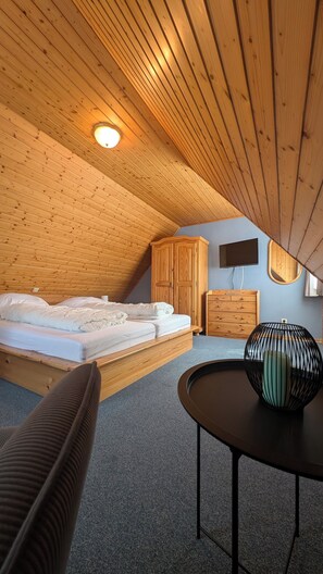 A bedroom with a sloped ceiling, a bed, a wardrobe, a dresser, a round table, and a chair. - Vacation Rental in the Kreß Links Vacation Home (Sellin)