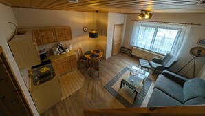 Um espaço de estar compacto com cozinha, área de jantar e sala de estar, com pisos e teto de madeira, uma mesa de jantar com cadeiras, um sofá e uma pequena mesa de centro.