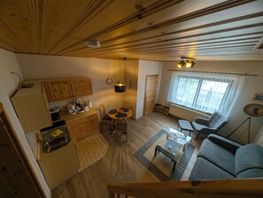A compact living space with a kitchen, dining area, and seating area, featuring wooden floors and ceiling, a dining table with chairs, a sofa, and a small coffee table. - Vacation Rental in the Kreß Links Vacation Home (Sellin)
