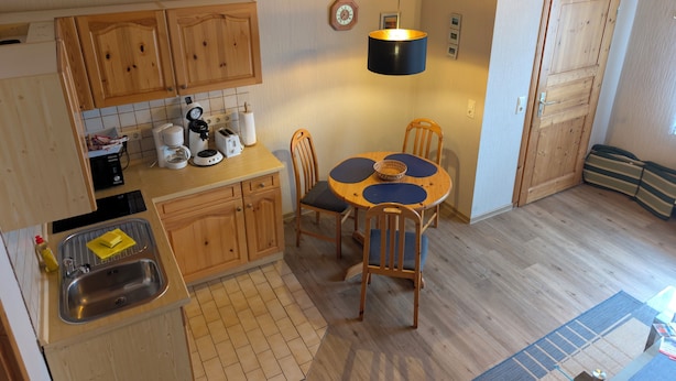 Uma cozinha compacta com armários de madeira, pia, mesa de jantar com cadeiras e luminária pendente.