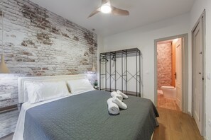 Hotelkamer met een bed, een plafondventilator, een bakstenen muur, een badkamer met een stenen muur, en een houten vloer.