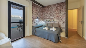 Un dormitorio con pared de ladrillo, una cama con almohadas, una silla y un ventilador de techo.