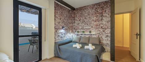 A bedroom with a brick wall, a bed with pillows, a chair, and a ceiling fan.