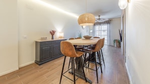 Comedor con mesa redonda, sillas, lámpara colgante y zona de cocina con armario y encimera.
