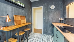 Una cocina moderna con una mesa de madera, taburetes de bar, una lámpara colgante y un reloj en la pared.