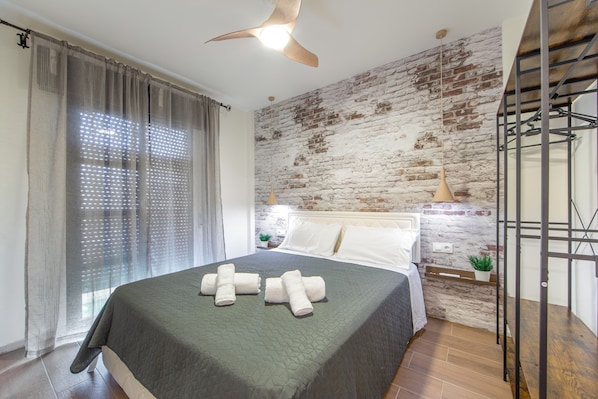 A bedroom with a bed, a ceiling fan, a brick wall, and a window with curtains.