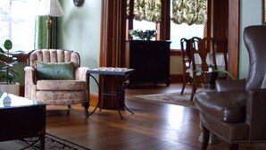 A living room with a sofa, armchair, and a small table. There is a window with curtains, a lamp, and a hanging decoration. - A La Gallarie Bed and Breakfast  (Niagara-on-the-Lake)