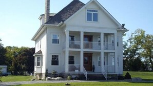 A two-story white house with a front porch, a chimney, and a small garden. - A La Gallarie Bed and Breakfast  (Niagara-on-the-Lake)