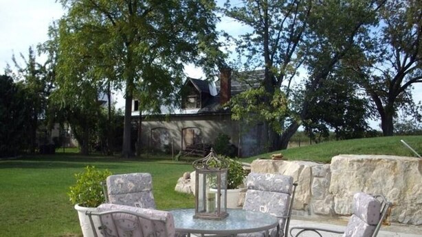 An outdoor patio with a round table and four chairs, surrounded by a stone wall and greenery. - A La Gallarie Bed and Breakfast  (Niagara-on-the-Lake)