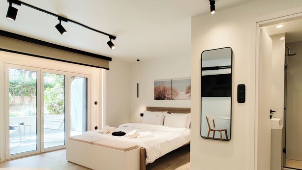 Ein modernes Schlafzimmer mit einem Bett, einem großen Spiegel und einer Glasschiebetür zu einem Außenbereich.