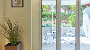 Ein Zimmer mit einer Glasschiebetür, die auf eine Terrassenanlage mit Stühlen und einem Blumentopf führt.