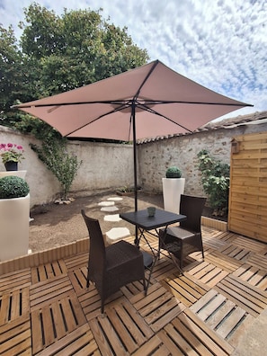 Une terrasse extérieure avec une table et des chaises, un grand parasol et des plantes en pot.