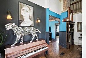 Ein Zimmer mit Klavier, einer dekorativen Tierfigur, einem gerahmten Porträt und einem Bücherregal.