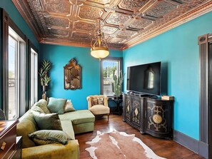Ein Wohnzimmer mit einer türkisfarbenen Wand, einer Holzbalkendecke, einem Sofa, einem Fernseher und einem Schrank.