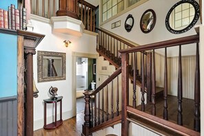 A grand staircase with a wooden railing, a wall adorned with framed mirrors, and a collection of books on a shelf. - Ravenwolf House - Odd & Elegant Downtown ABQ Gem (Albuquerque)