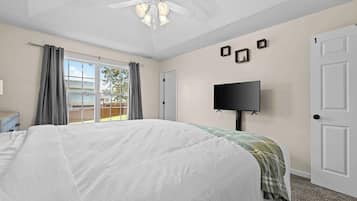 A bedroom with a large bed, a ceiling fan, a flat-screen TV, and a window with curtains.
